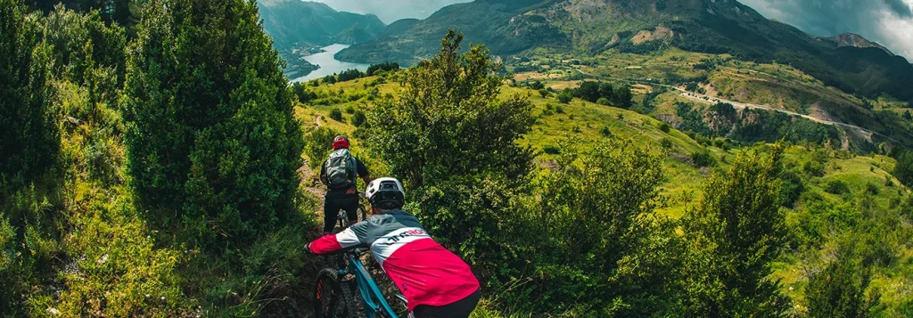 Ciclistas recorren un sendero monta&ntilde;oso con vista a un lago en un paisaje verde.