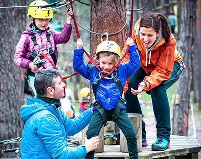 Ni&ntilde;os y adultos disfrutando de un circuito de cuerdas en el bosque.