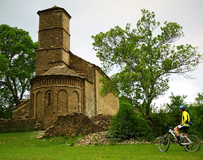 Ciclista pasa frente a una antigua iglesia de piedra rodeada de &aacute;rboles.