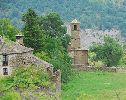 Iglesia y casas de piedra rodeadas de vegetaci&oacute;n y monta&ntilde;as.