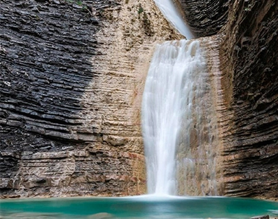 Cascada cayendo entre rocas en una piscina natural de agua turquesa.