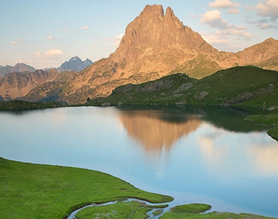 Monta&ntilde;a reflejada en el lago con vegetaci&oacute;n verde y cielo azul.