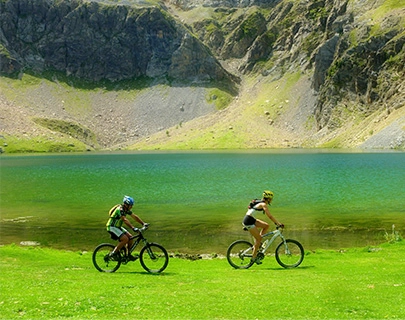 Ciclistas junto a un lago verde esmeralda y monta&ntilde;as al fondo.