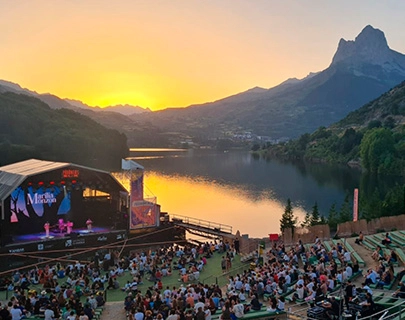 Concierto al aire libre al atardecer junto a un lago y monta&ntilde;as.