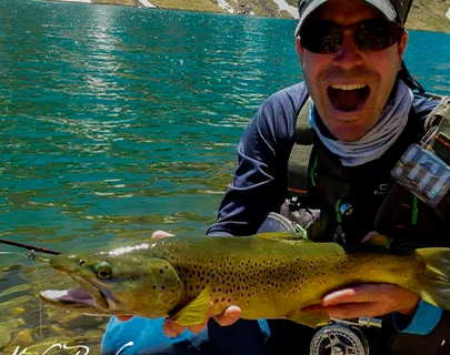 Persona sonriente sosteniendo un gran pez frente a un lago.