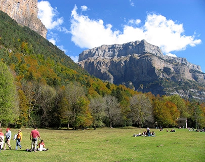 Personas disfrutando de un d&iacute;a soleado en un parque con monta&ntilde;as al fondo.