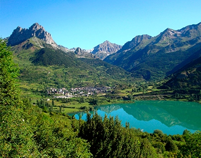 Monta&ntilde;as verdes y un lago turquesa reflejan un cielo azul claro.