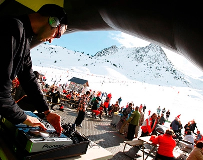 DJ tocando en una fiesta al aire libre en la nieve, gente disfrutando alrededor.