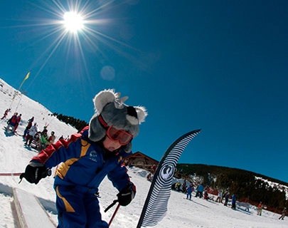 Ni&ntilde;o esquiando con disfraz de oso bajo un cielo soleado.