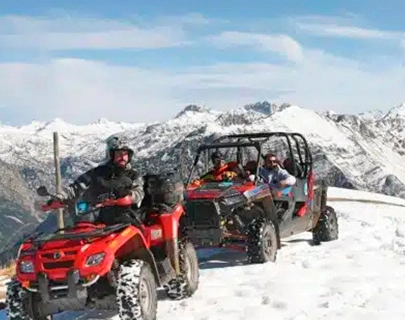 Personas manejando cuatrimotos en la nieve con monta&ntilde;as al fondo.