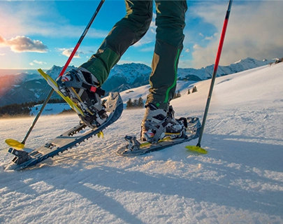 Persona con raquetas de nieve en monta&ntilde;a con bastones al atardecer.