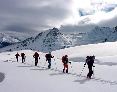 Personas esquiando en fila en una monta&ntilde;a nevada bajo un cielo parcialmente nublado.