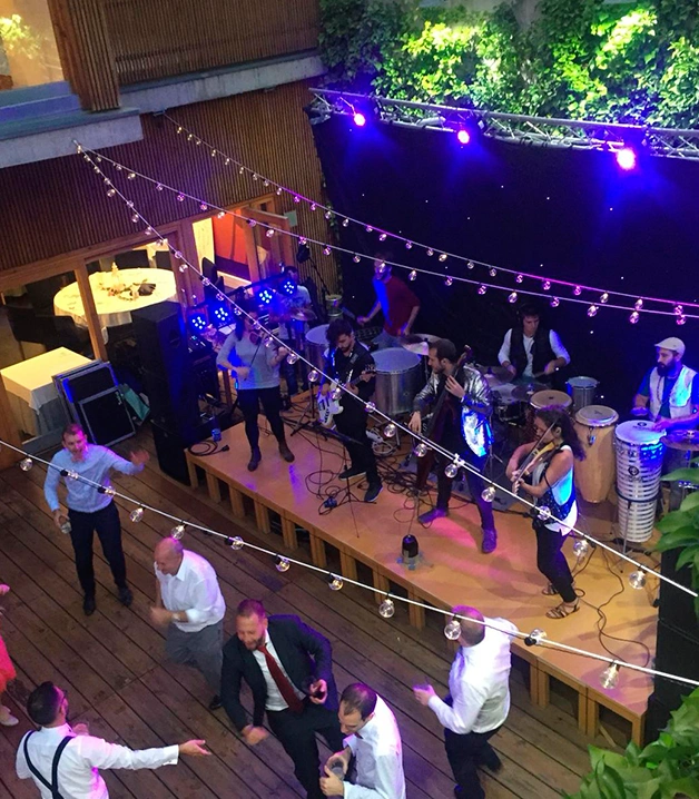 Concierto en vivo con gente bailando, luces p&uacute;rpuras y decoraciones colgantes.