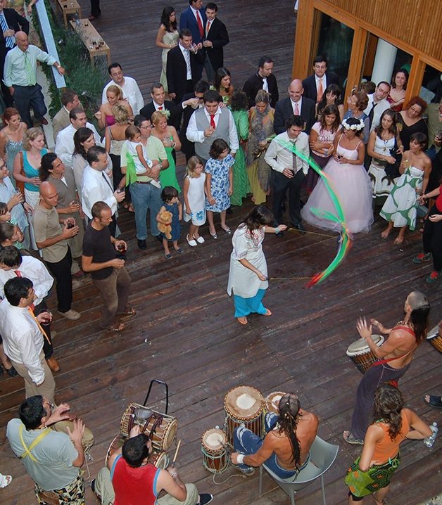 Grupo de personas observando danza con cintas y percusi&oacute;n en una fiesta.