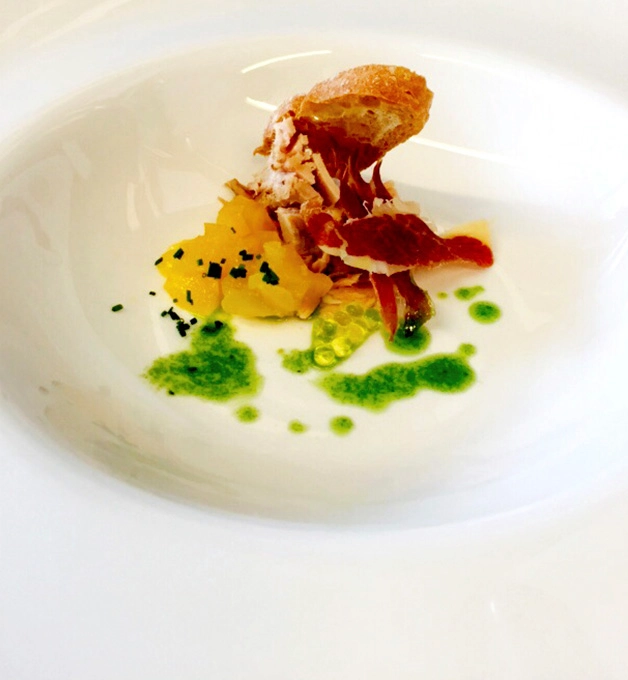 Plato gourmet con jam&oacute;n, pur&eacute; y salsa verde sobre plato blanco.