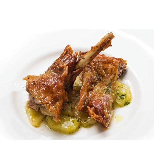 Plato de cordero asado con papas en un plato blanco.