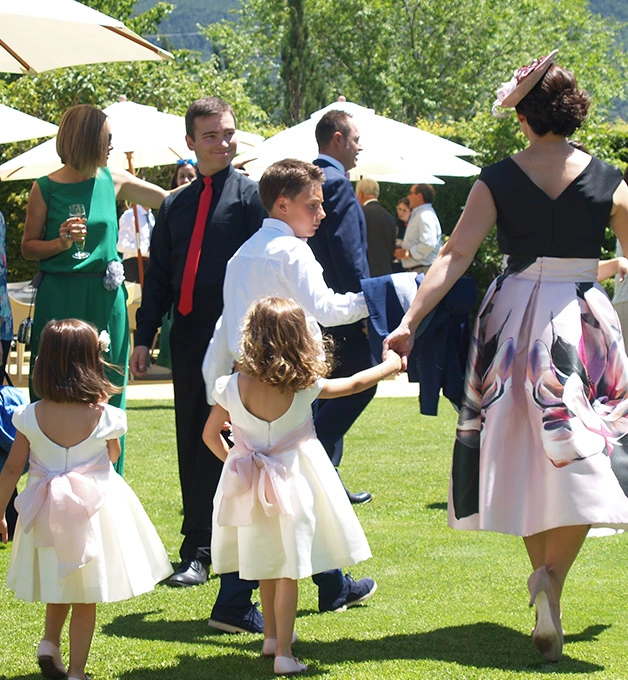 Personas elegantes caminando en una reuni&oacute;n al aire libre bajo sombrillas.