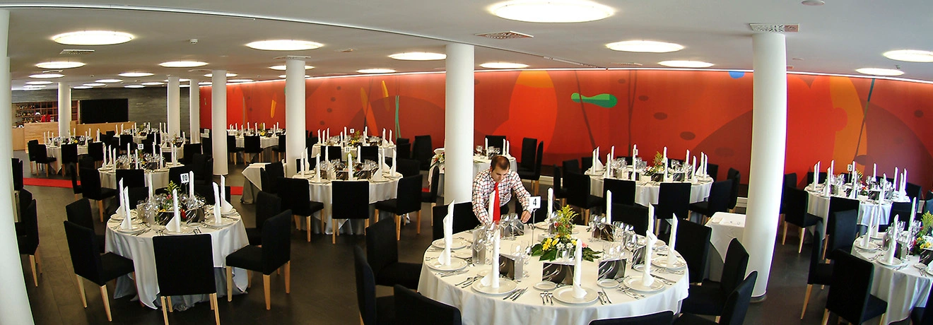 Sal&oacute;n con mesas redondas elegantes, cubiertos y sillas negras, decorado moderno.