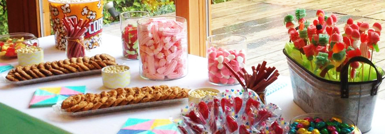 Mesa con dulces variados, galletas y palomitas en envases de vidrio y metal.