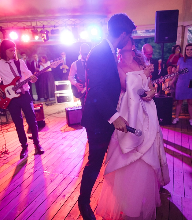 Pareja bes&aacute;ndose en una boda con m&uacute;sica en vivo de fondo.