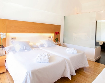 Habitaci&oacute;n moderna con dos camas, iluminaci&oacute;n suave y flores decorativas.