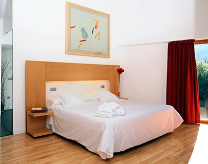 Habitaci&oacute;n moderna con cama blanca, pintura abstracta y cortinas rojas.