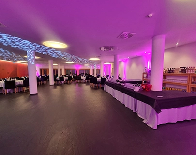 Sala de eventos con iluminaci&oacute;n violeta y mesas preparadas.