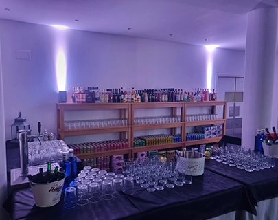 Barra de bebidas con botellas, vasos y estantes iluminados.