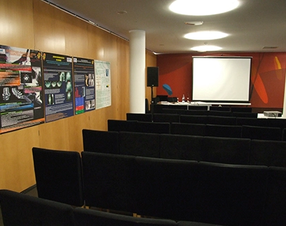 Sala de conferencias vac&iacute;a con sillas negras y pantalla de proyecci&oacute;n al frente.