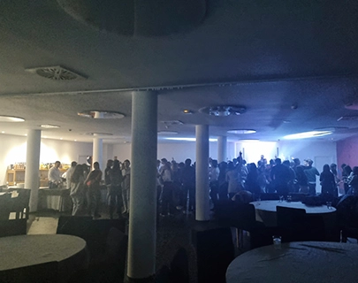 Una multitud reunida en un sal&oacute;n oscuro con mesas vac&iacute;as en primer plano.