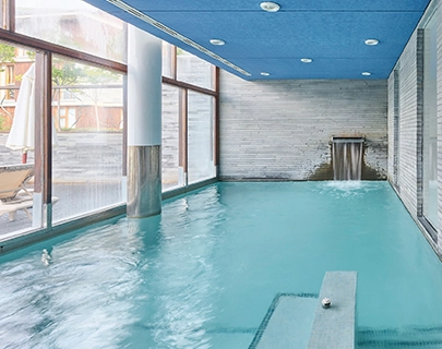 Piscina techada con cascada, rodeada de ventanas amplias y paredes grises.