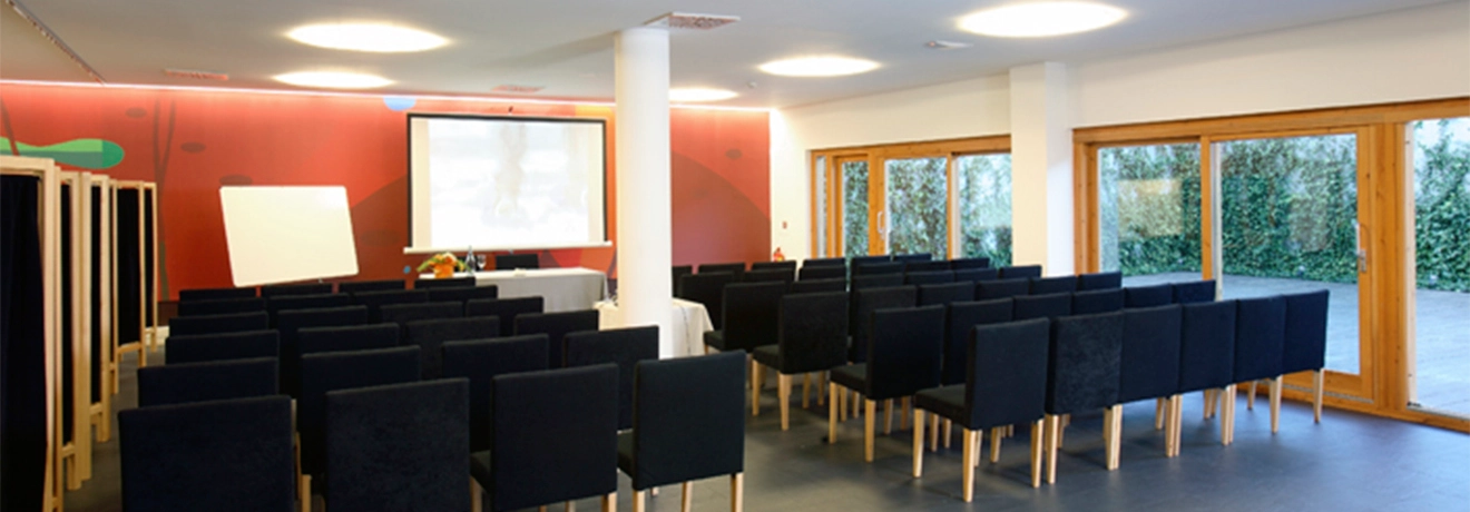 Sala de conferencias con sillas negras y pantalla blanca.