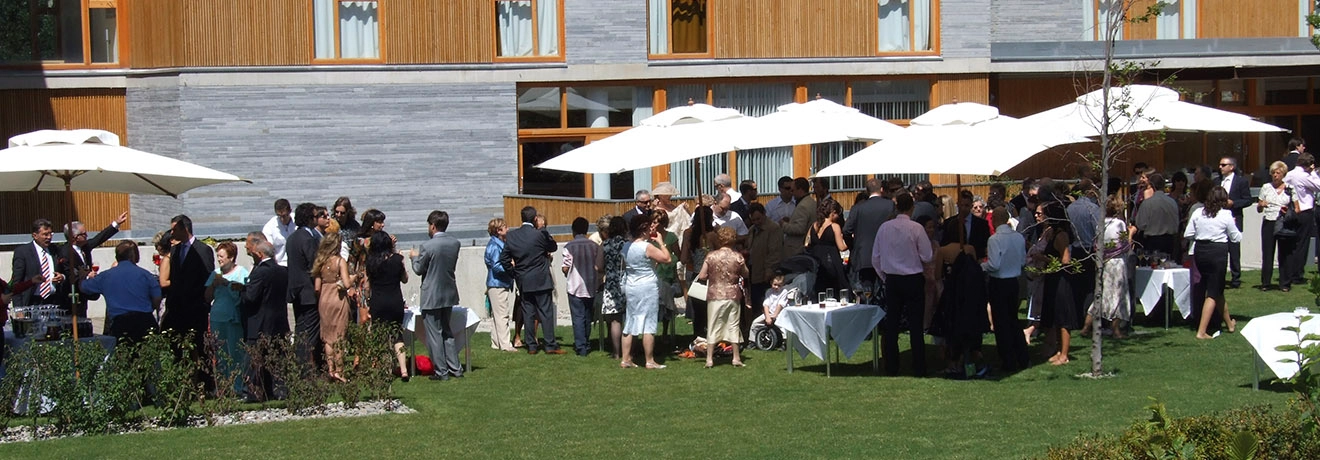 Personas reunidas en un evento al aire libre, con mesas y sombrillas blancas.