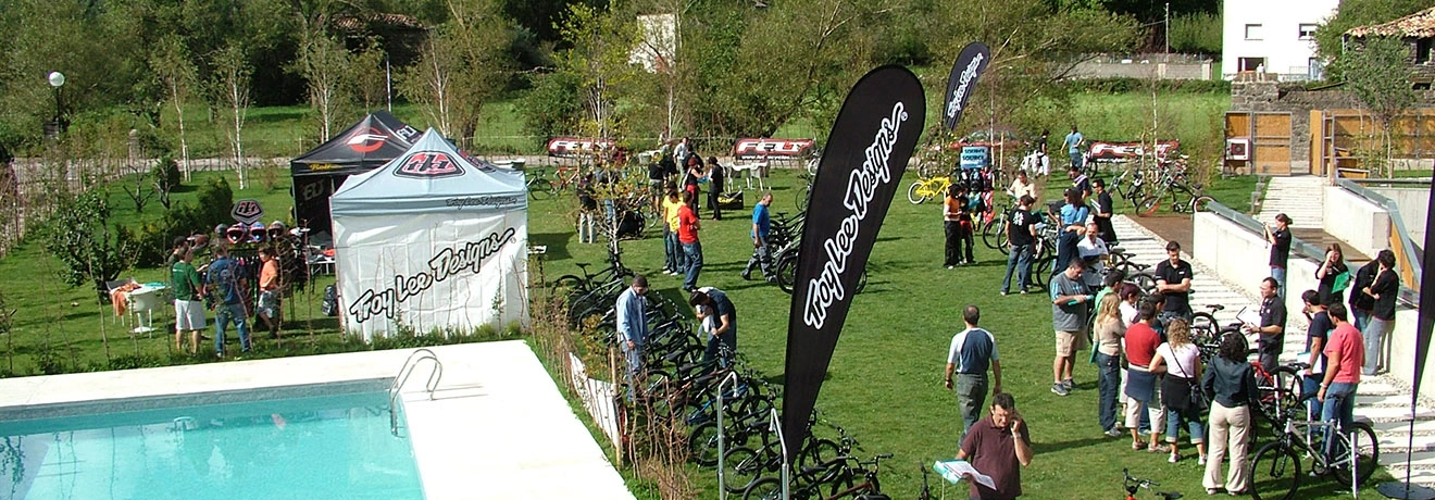 Evento al aire libre de ciclismo con tiendas, bicicletas y gente en un jard&iacute;n.