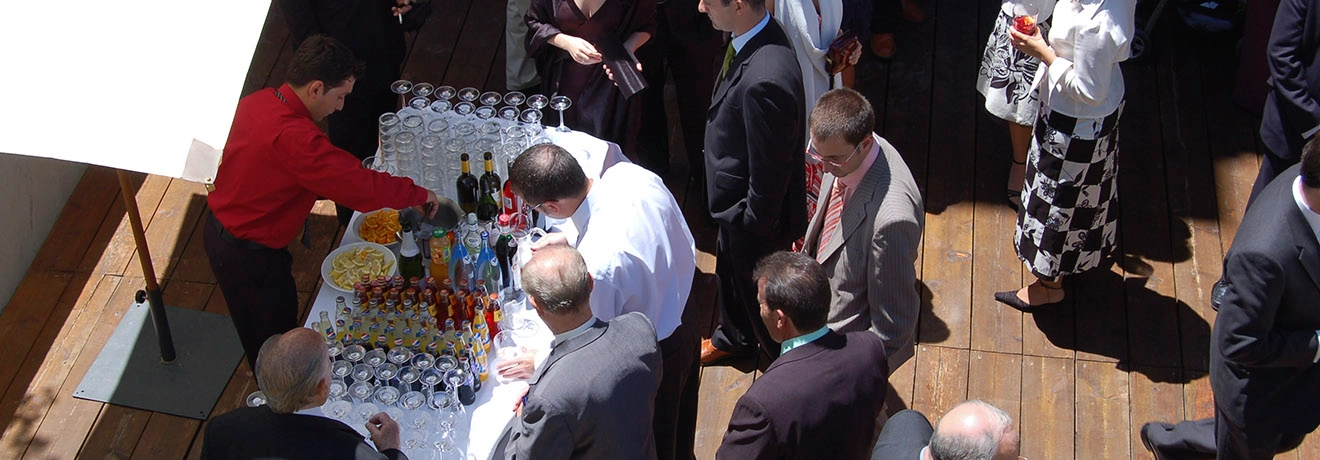 Personas reunidas en torno a una mesa con bebidas y aperitivos en un evento.