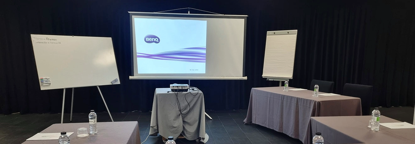 Sala de conferencias con proyector, pizarras y mesas con botellas de agua.