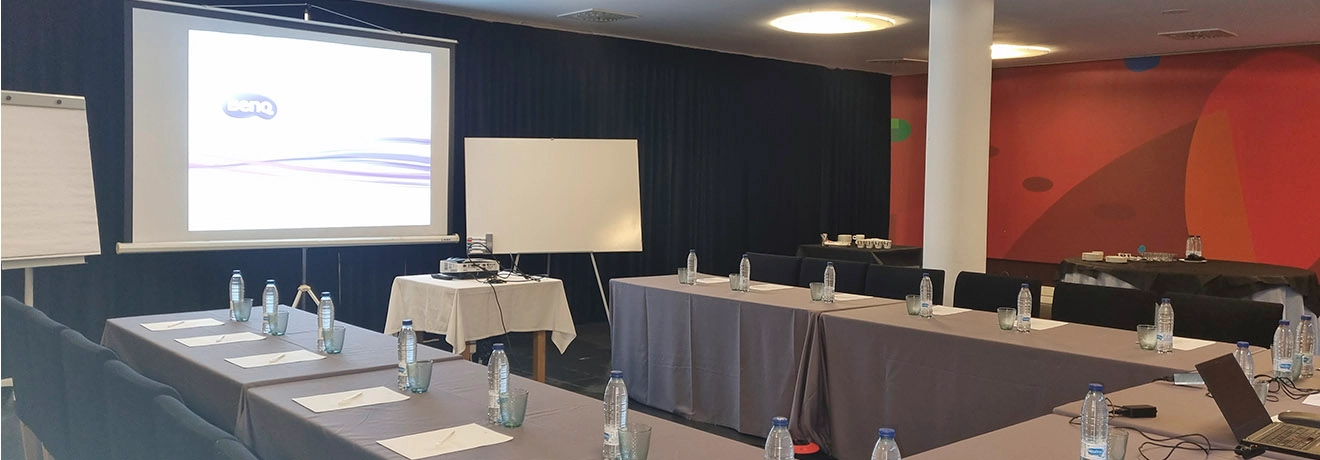 Sala de conferencias lista con proyector, pizarra y mesas dispuestas en forma de U.