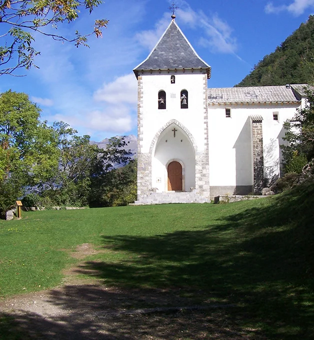 Iglesia blanca con campanario rodeada de naturaleza y cielo azul.