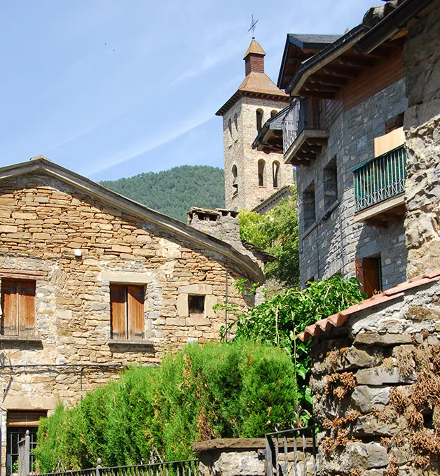 Edificios de piedra y una torre con campanario en un entorno monta&ntilde;oso.
