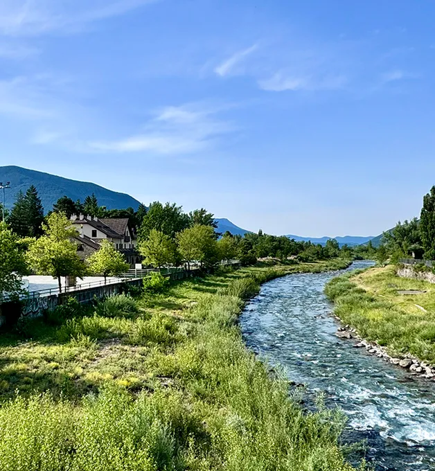 R&iacute;o rodeado de vegetaci&oacute;n, casas y &aacute;rboles en un paisaje monta&ntilde;oso.