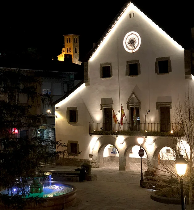 Edificio iluminado de noche con fuente en primer plano y torre al fondo.