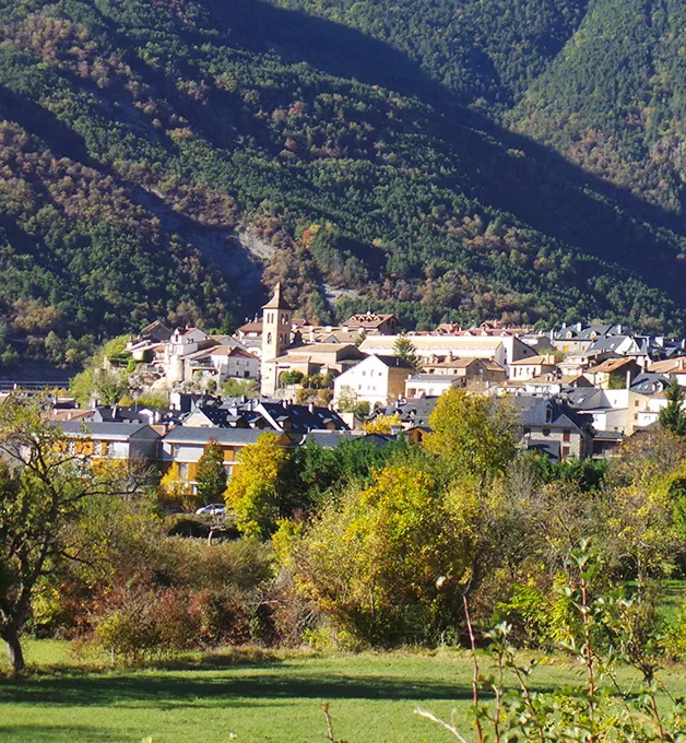 Pueblo rodeado de monta&ntilde;as y vegetaci&oacute;n en un d&iacute;a soleado.