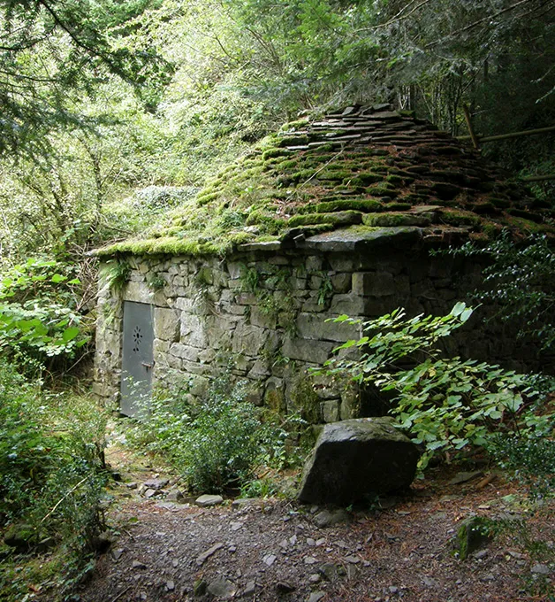 Caba&ntilde;a de piedra cubierta de musgo en un bosque frondoso.
