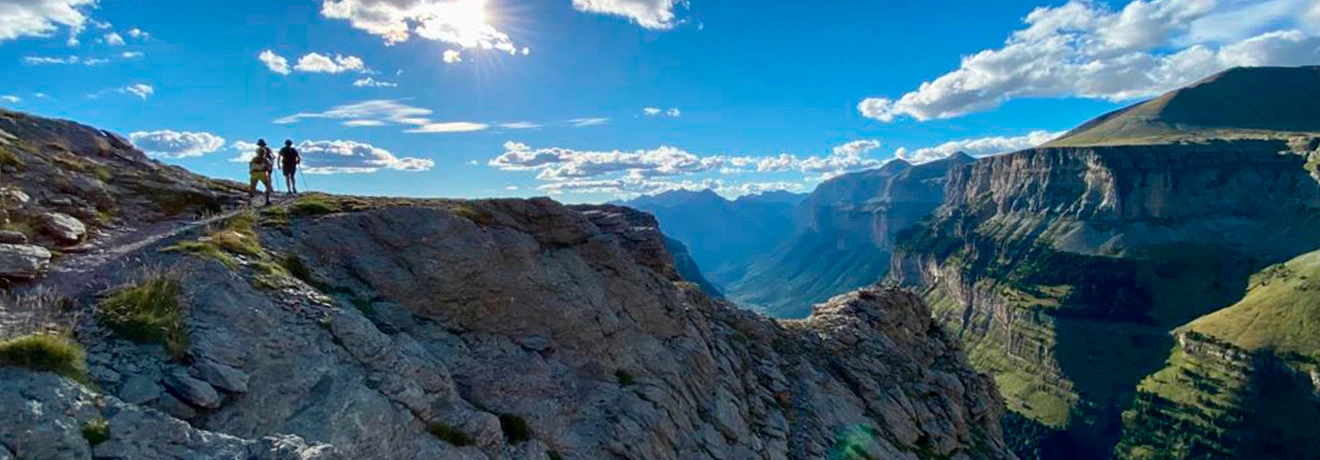 Excursionistas en un escarpado acantilado con un paisaje monta&ntilde;oso al fondo.