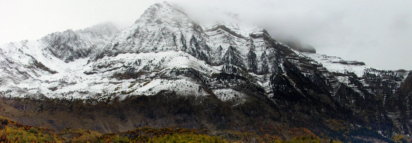 Monta&ntilde;a nevada con cielo nublado y bosque en el inicio del oto&ntilde;o.