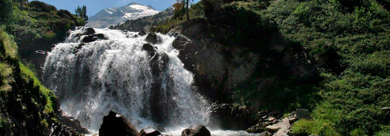 Cascada en un paisaje verde con monta&ntilde;as nevadas al fondo.