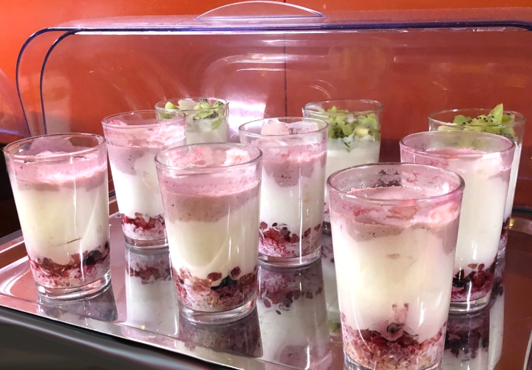Vasos con capas de yogur, granola y frutas en una bandeja rectangular.