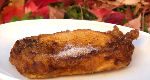 Plato con una tostada francesa espolvoreada con az&uacute;car. Fondo de hojas rojas.