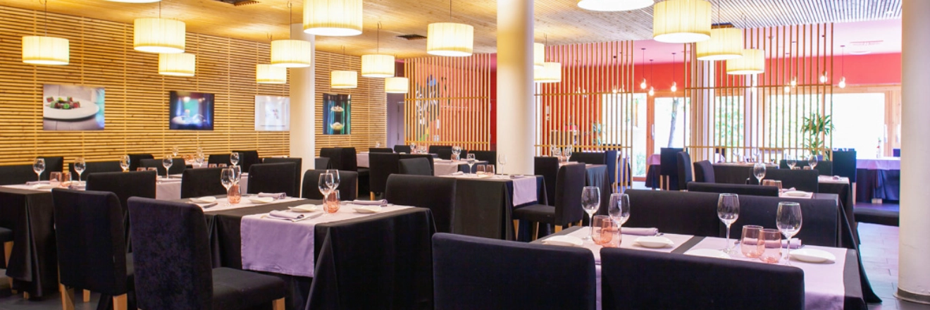 Restaurante elegante con mesas vestidas, luces colgantes y decoraci&oacute;n moderna.