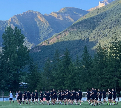 Grupo de personas entrenando en un campo rodeado de monta&ntilde;as y &aacute;rboles.